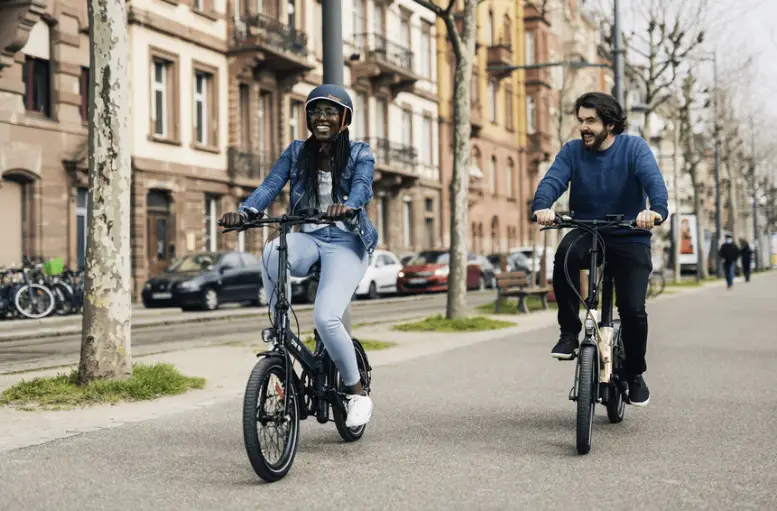 two people riding folding electric bikes in a city